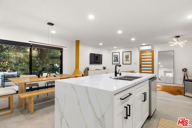 kitchen with white cabinets, light stone counters, sink, and an island with sink