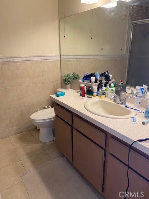 bathroom featuring tile patterned flooring, vanity, toilet, and tile walls