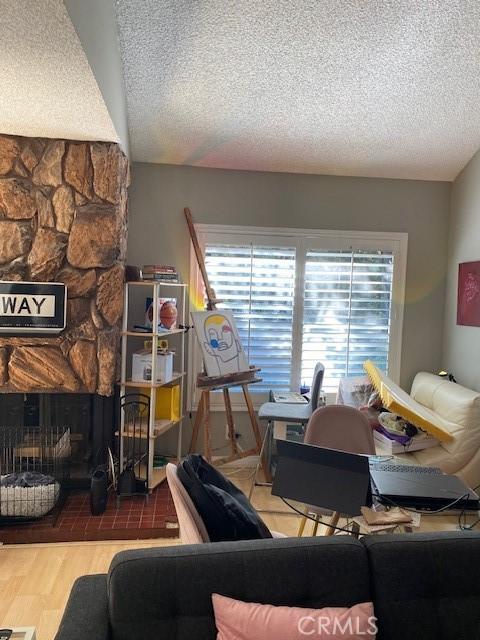 living room with a stone fireplace, a textured ceiling, and hardwood / wood-style flooring