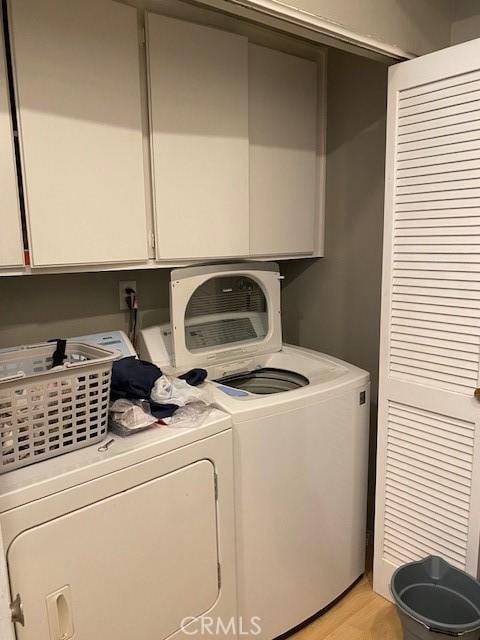 washroom with washing machine and clothes dryer, cabinets, and light wood-type flooring