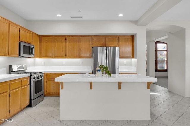 kitchen with a center island, tile countertops, stainless steel appliances, recessed lighting, and visible vents