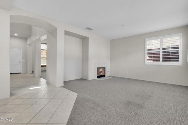 unfurnished living room featuring arched walkways, a fireplace, light carpet, and a healthy amount of sunlight