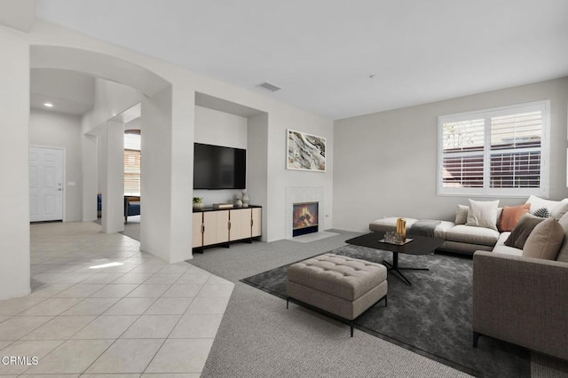 living room featuring arched walkways, visible vents, light carpet, light tile patterned flooring, and a tile fireplace