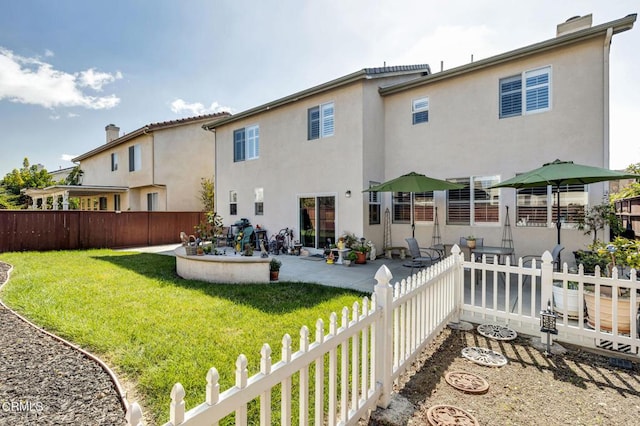 rear view of property featuring fence private yard, a yard, stucco siding, and a patio