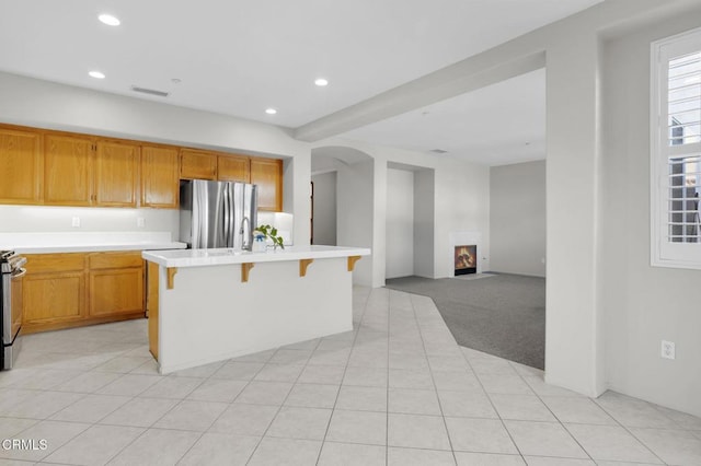 kitchen with light carpet, appliances with stainless steel finishes, a breakfast bar area, a lit fireplace, and light countertops