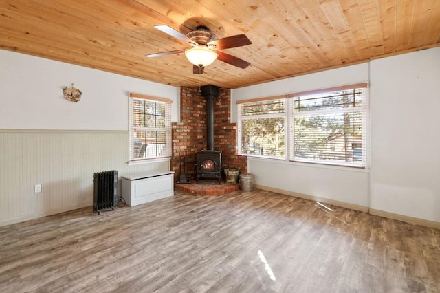 unfurnished living room featuring wooden ceiling, wood-type flooring, radiator, and a wood stove