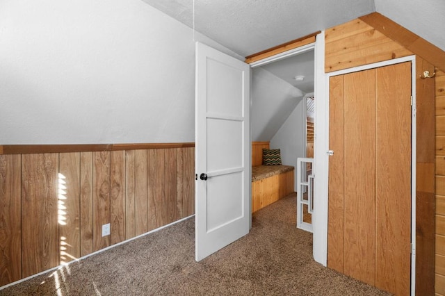 bonus room with a textured ceiling, wooden walls, vaulted ceiling, and dark colored carpet