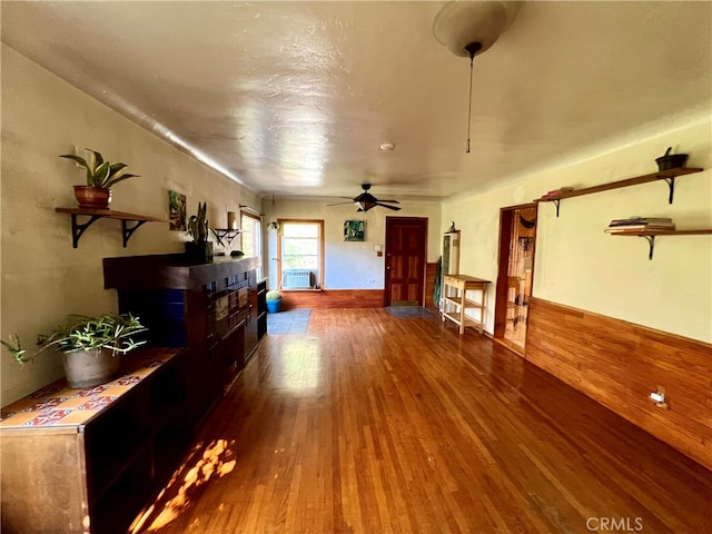 unfurnished living room featuring wood-type flooring, wooden walls, and ceiling fan