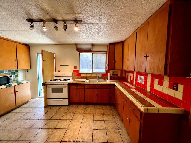 kitchen featuring white gas range, sink, tile counters, and track lighting