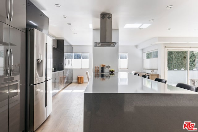 kitchen with a large island, island range hood, a wealth of natural light, and stainless steel refrigerator with ice dispenser