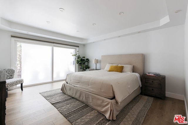 bedroom with wood-type flooring, access to exterior, and a tray ceiling