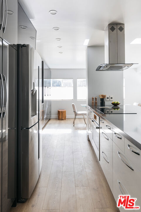 kitchen featuring stainless steel fridge, island exhaust hood, black electric stovetop, light hardwood / wood-style floors, and white cabinets