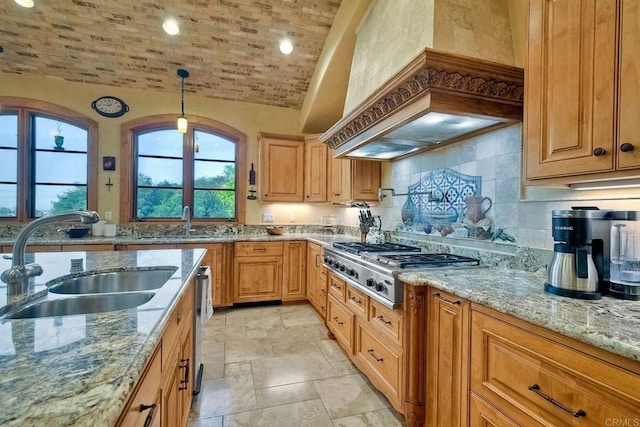 kitchen with sink, stainless steel gas stovetop, light stone counters, decorative light fixtures, and vaulted ceiling