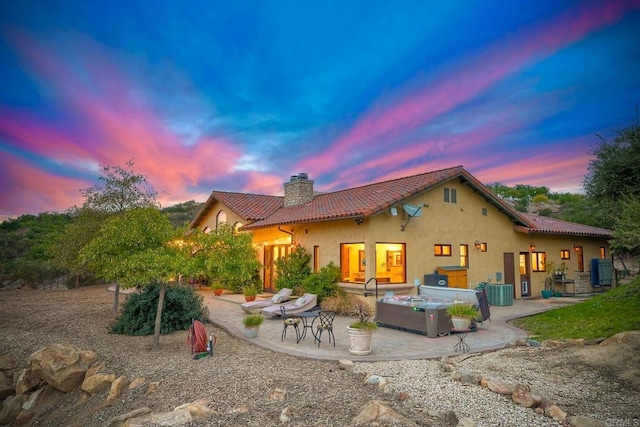 back house at dusk with a patio, a hot tub, and central air condition unit