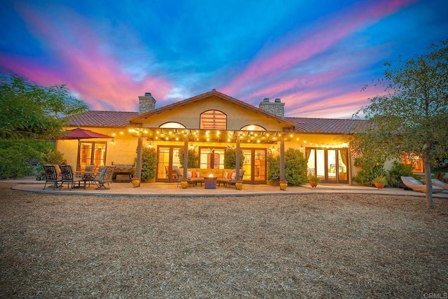 back house at dusk featuring outdoor lounge area, french doors, and a patio