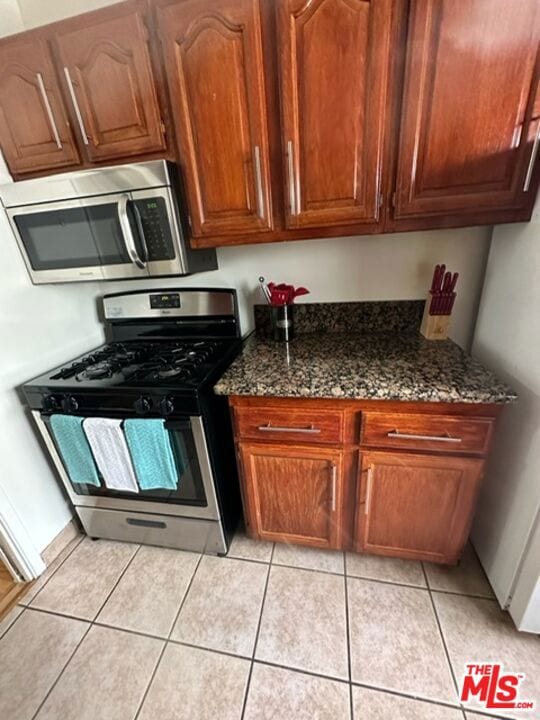 kitchen featuring light tile patterned floors, stainless steel appliances, and dark stone counters