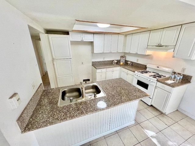 kitchen featuring white gas range, sink, white cabinets, and dark stone counters