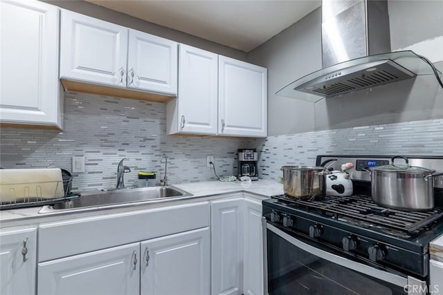 kitchen featuring wall chimney exhaust hood, stainless steel gas stove, white cabinetry, and tasteful backsplash