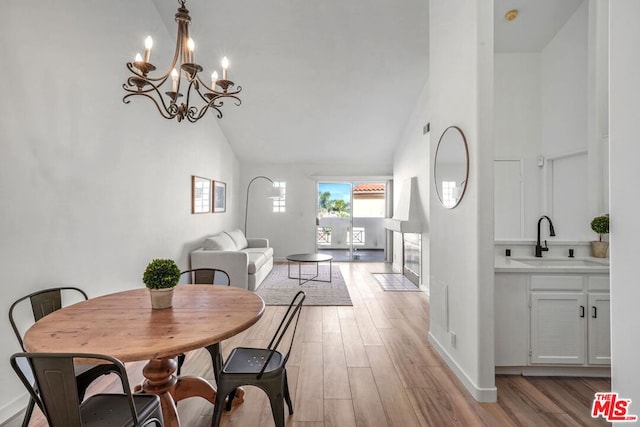 dining room featuring sink, high vaulted ceiling, an inviting chandelier, and light wood-type flooring