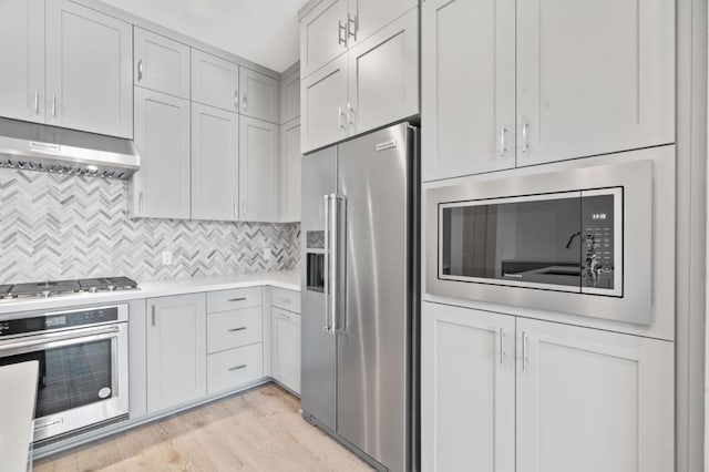 kitchen with exhaust hood, appliances with stainless steel finishes, light hardwood / wood-style floors, and backsplash