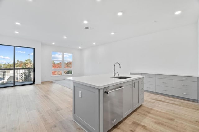 kitchen featuring gray cabinets, a center island with sink, stainless steel dishwasher, sink, and light hardwood / wood-style flooring