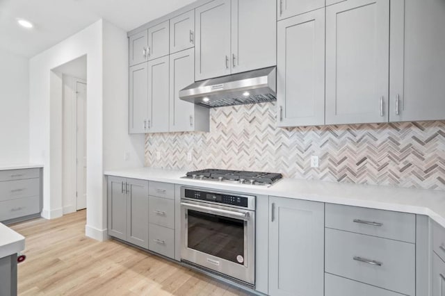 kitchen with backsplash, gray cabinets, stainless steel appliances, and light hardwood / wood-style flooring