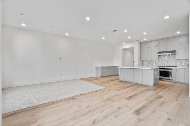 kitchen featuring range, tasteful backsplash, an island with sink, stainless steel oven, and light hardwood / wood-style flooring