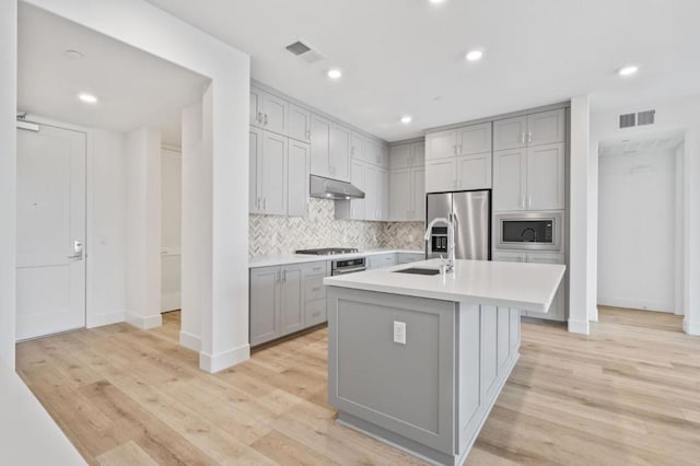 kitchen with gray cabinets, sink, light hardwood / wood-style flooring, a kitchen island with sink, and stainless steel appliances