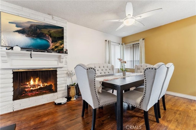 dining area with ceiling fan, hardwood / wood-style floors, a textured ceiling, and a brick fireplace