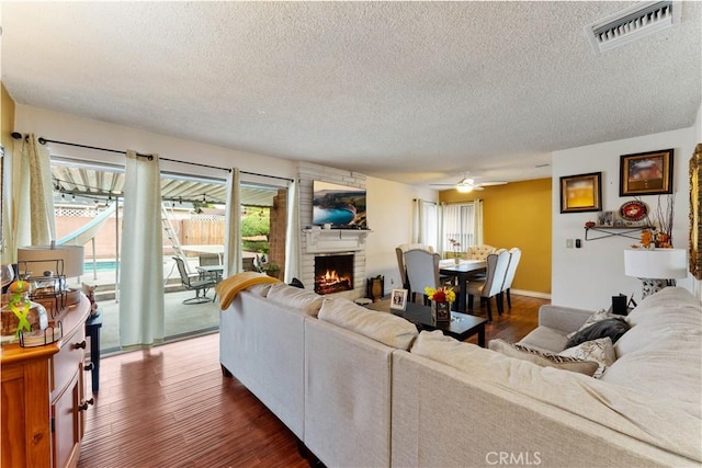 living room featuring a fireplace, a textured ceiling, dark hardwood / wood-style floors, and ceiling fan