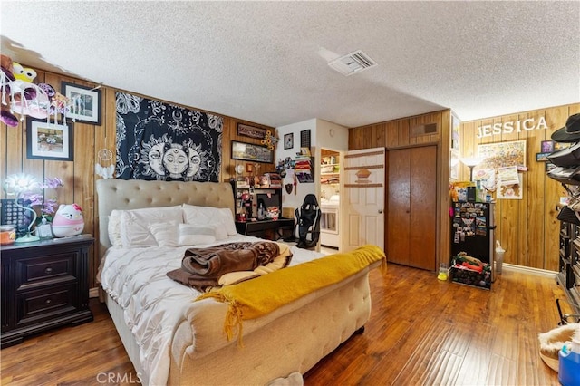 bedroom with hardwood / wood-style floors, a textured ceiling, and wooden walls