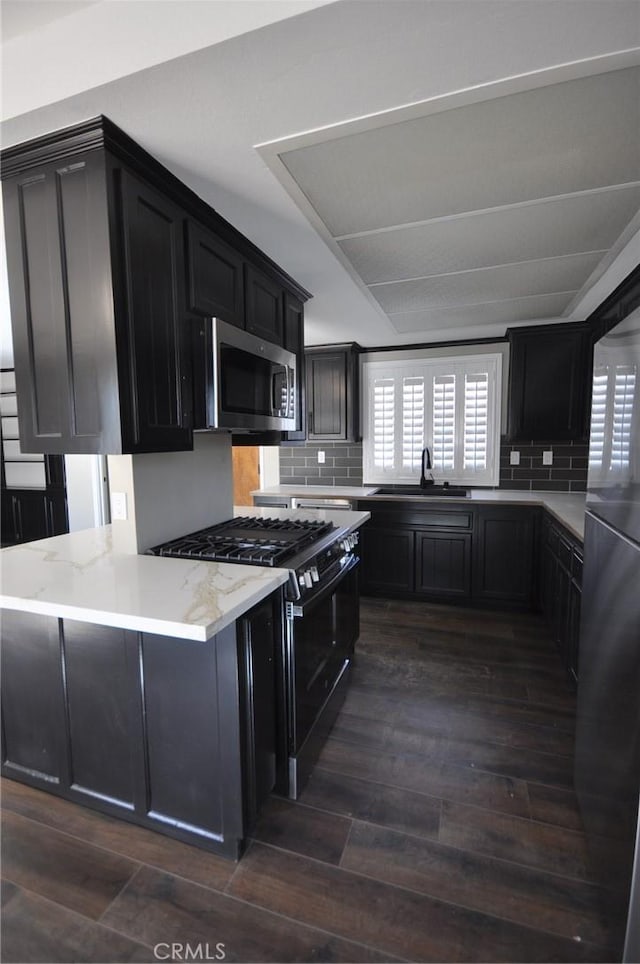 kitchen featuring sink, dark hardwood / wood-style floors, tasteful backsplash, gas range, and kitchen peninsula