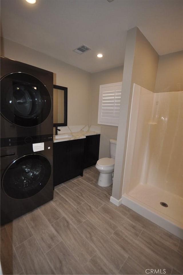 bathroom with vanity, toilet, a shower, and stacked washing maching and dryer