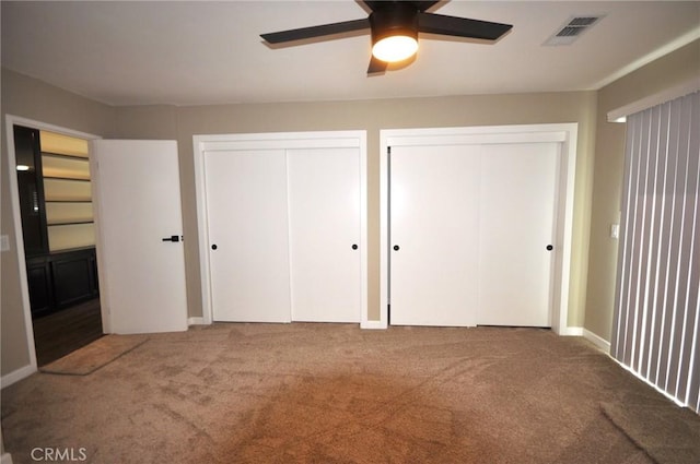 unfurnished bedroom with ceiling fan, carpet, and two closets