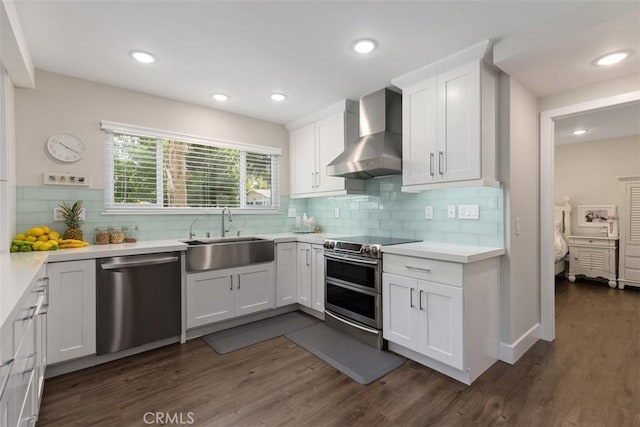 kitchen featuring white cabinetry, appliances with stainless steel finishes, decorative backsplash, wall chimney range hood, and sink