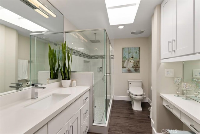 bathroom featuring toilet, vanity, wood-type flooring, a shower with shower door, and a skylight