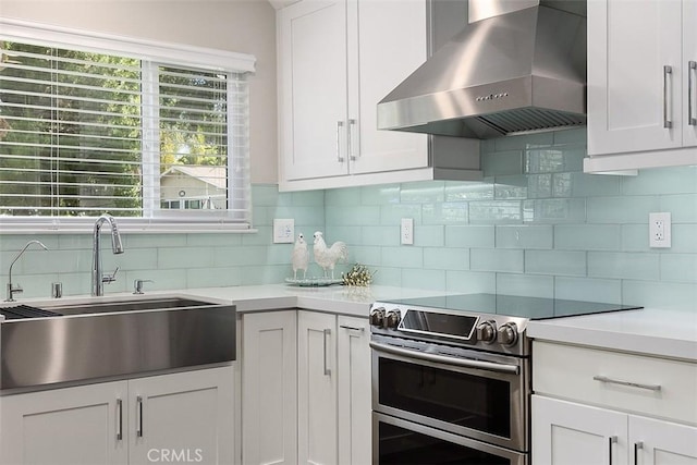 kitchen featuring range hood, decorative backsplash, sink, white cabinetry, and range with two ovens