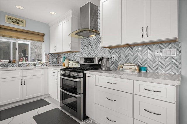 kitchen featuring decorative backsplash, sink, wall chimney range hood, range with two ovens, and white cabinets