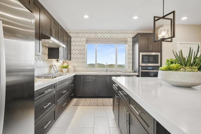 kitchen with pendant lighting, backsplash, sink, appliances with stainless steel finishes, and dark brown cabinetry