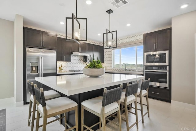 kitchen with backsplash, dark brown cabinets, stainless steel appliances, a center island, and hanging light fixtures