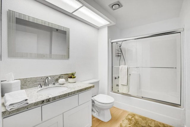 full bathroom featuring toilet, combined bath / shower with glass door, hardwood / wood-style flooring, and vanity