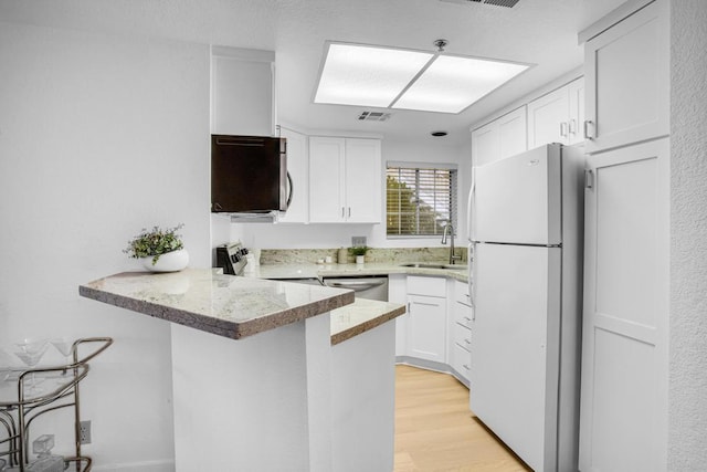 kitchen with white fridge, kitchen peninsula, sink, white cabinets, and range