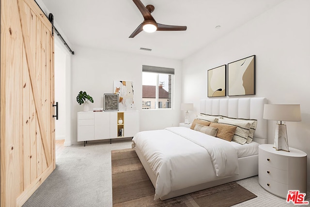 bedroom featuring light carpet, a barn door, and ceiling fan