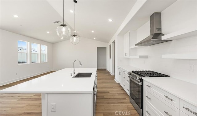 kitchen with stainless steel gas stove, a sink, wall chimney exhaust hood, light wood-style flooring, and lofted ceiling