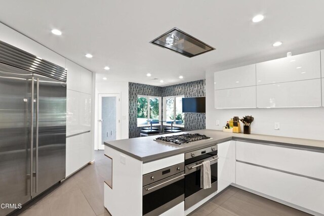 kitchen featuring kitchen peninsula, white cabinets, light tile patterned flooring, and appliances with stainless steel finishes