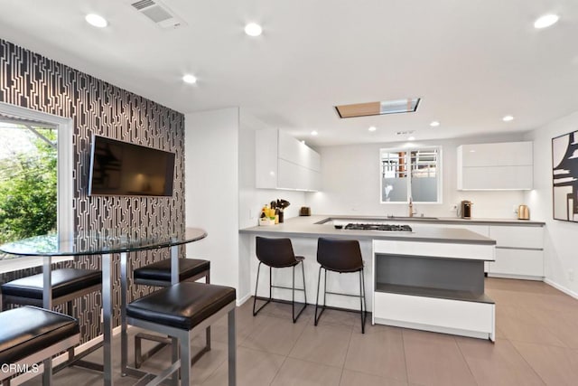 kitchen featuring kitchen peninsula, a breakfast bar, white cabinets, and light tile patterned flooring