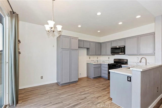 kitchen featuring gray cabinetry, pendant lighting, light wood-type flooring, a notable chandelier, and gas stove