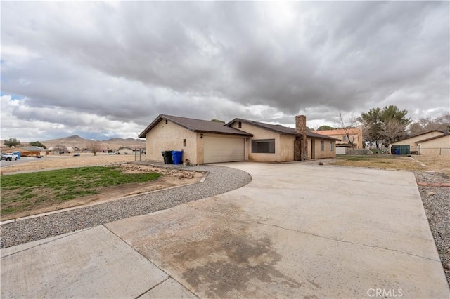 view of side of property featuring stucco siding, a chimney, concrete driveway, and an attached garage