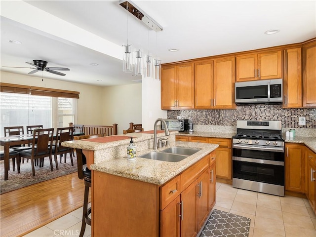 kitchen with sink, appliances with stainless steel finishes, a kitchen island with sink, a kitchen breakfast bar, and decorative light fixtures