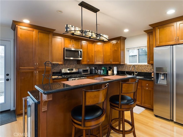 kitchen with pendant lighting, backsplash, stainless steel appliances, light hardwood / wood-style floors, and a kitchen island